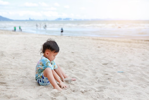 Portrait de petit garçon asiatique s'amusant avec du sable à la plage