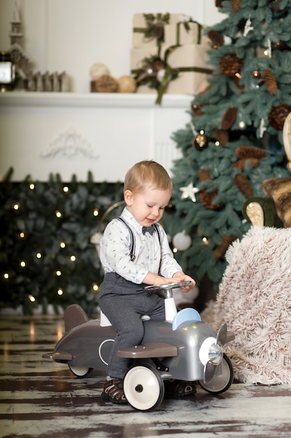 Portrait d'un petit garçon assis sur un avion jouet vintage près d'un arbre de Noël