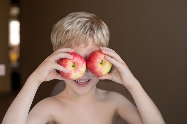 Portrait d'un petit garçon blond avec des pommes rouges mûres dans les mains, il sourit, il s'amuse.