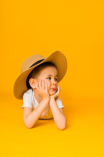 Portrait d'un petit garçon dans un chapeau de paille couché sur une surface jaune et à l'écart