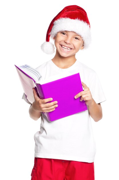 Portrait d'un petit garçon heureux en bonnet de Noel avec livre isolé sur fond blanc