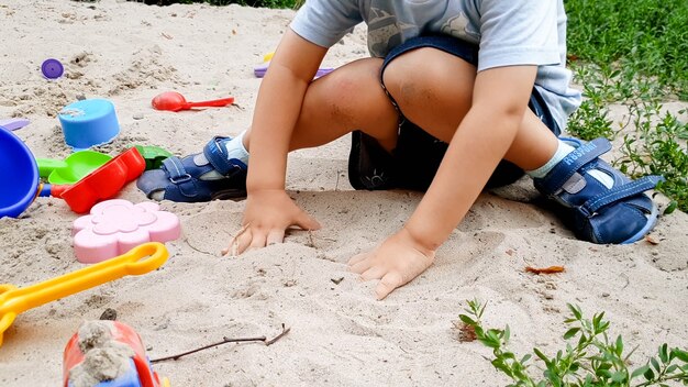 Portrait d'un petit garçon jouant avec des jouets et creusant du sable dans un bac à sable au parc