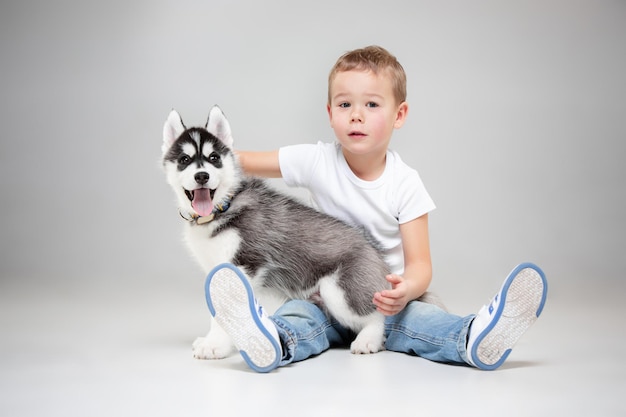 Portrait d'un petit garçon joyeux s'amusant avec un chiot husky sibérien sur le sol au studio.