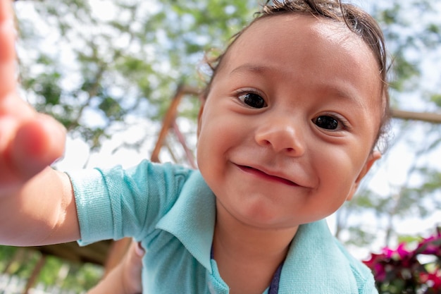 Portrait d'un petit garçon latin essayant de prendre un selfie Joli bébé veut toucher l'appareil photo en souriant