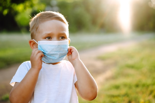 Portrait de petit garçon avec masque médical dans le parc.