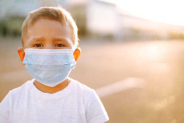 Portrait de petit garçon avec masque médical regardant la caméra dans la ville