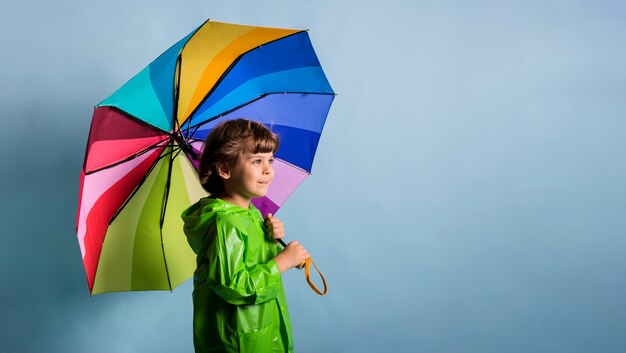 Portrait d'un petit garçon avec un parapluie multicolore se dresse sur un fond bleu avec une place pour le texte