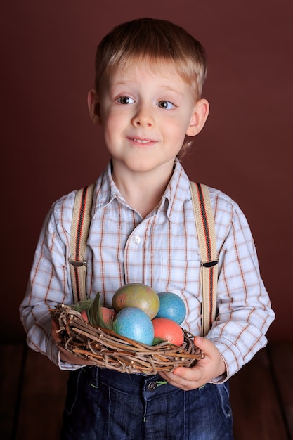 Portrait d'un petit garçon pensif avec un nid en osier dans ses mains et des oeufs de Pâques. Concept de Pâques