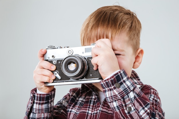 Portrait de petit garçon prenant des photos avec un vieil appareil photo vintage sur un mur blanc