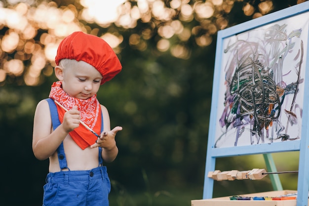 Portrait d'un petit garçon qui sourit d'embarras et se réjouit de la peinture dans ses mains