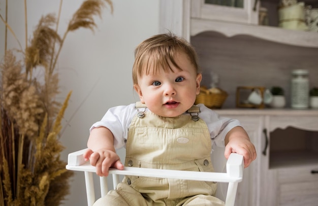 Portrait d'un petit garçon de race blanche dans une combinaison beige assis dans une chaise haute blanche dans la cuisine