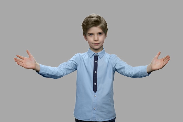 Portrait de petit garçon répandant les mains sur fond gris. Garçon enfant mignon écartant les mains accueillant ou saluant quelqu'un.