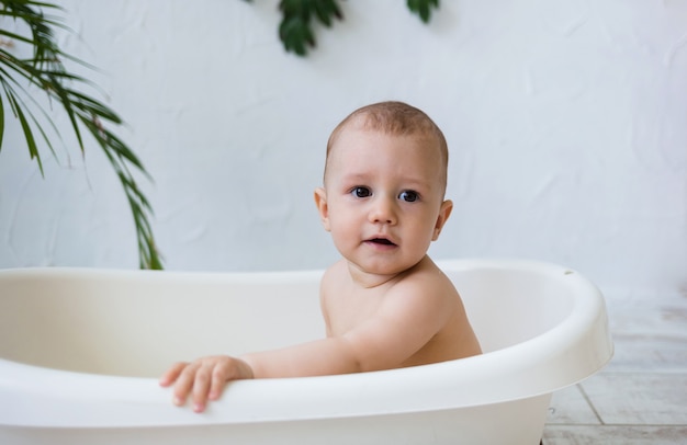 Portrait d'un petit garçon se baignant dans un bain blanc sur une surface blanche avec des plantes