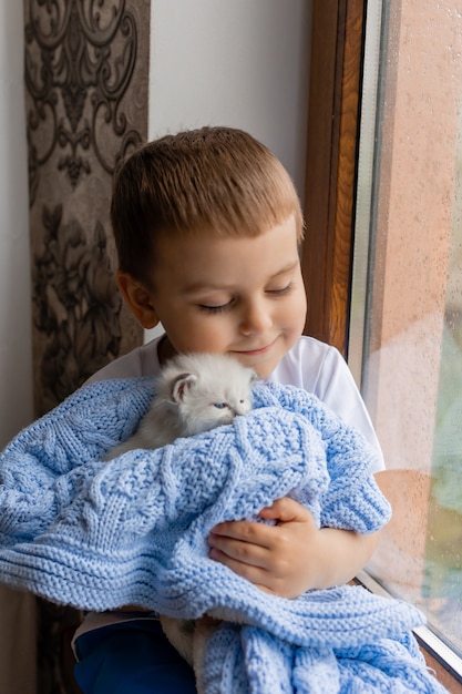 Portrait d'un petit garçon tenant un chaton blanc enveloppé dans une couverture tricotée bleue dans ses mains