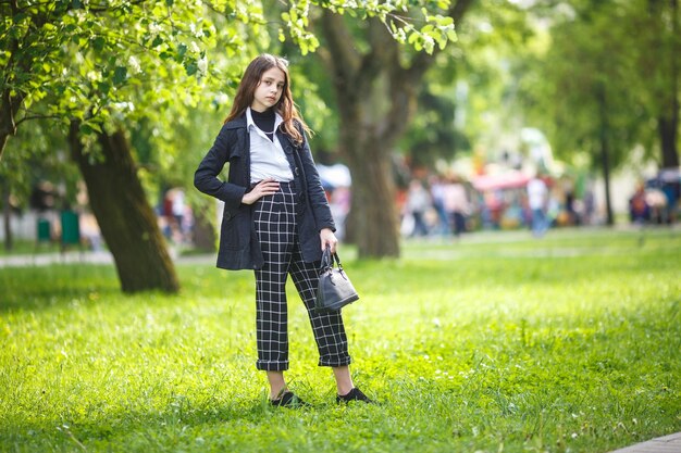 Portrait d'une petite belle fille élégante avec des lunettes de soleil et un pantalon court à carreaux dans le parc de la ville sur fond de forêt verte