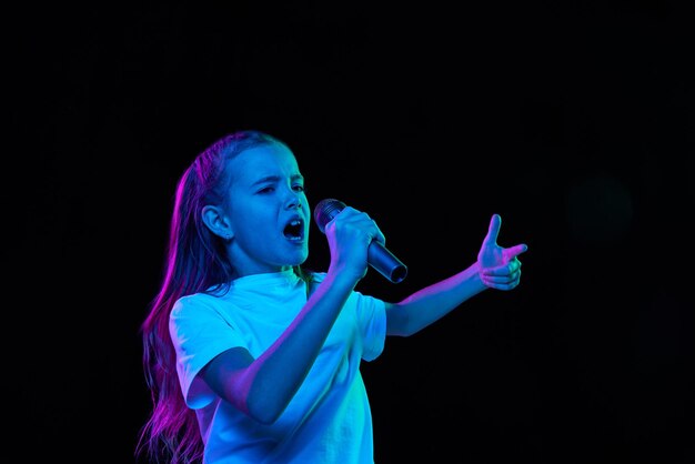 Portrait de petite belle fille enfant en t-shirt blanc posant chantant dans un microphone isolé sur