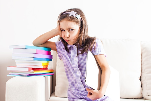 Portrait de petite écolière fatiguée qui s'appuie sur des livres scolaires colorés. Retour au concept de l'école