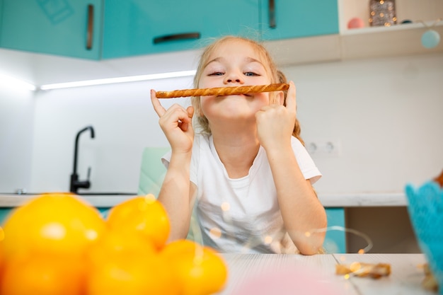 Portrait d'une petite fille de 7 ans assise dans la cuisine et jouant avec des gressins. L'enfant prend le petit déjeuner dans la cuisine