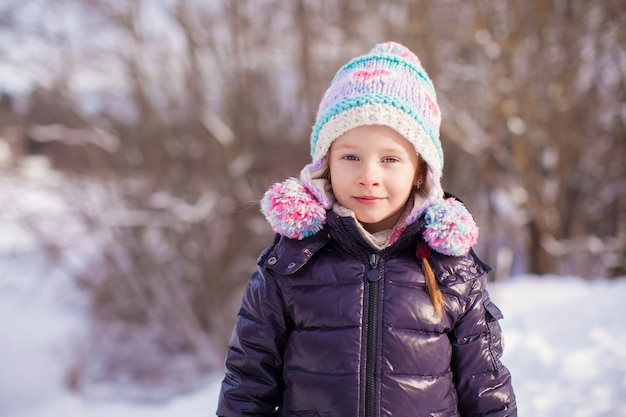 Portrait de petite fille adorable au chapeau d'hiver à la forêt enneigée