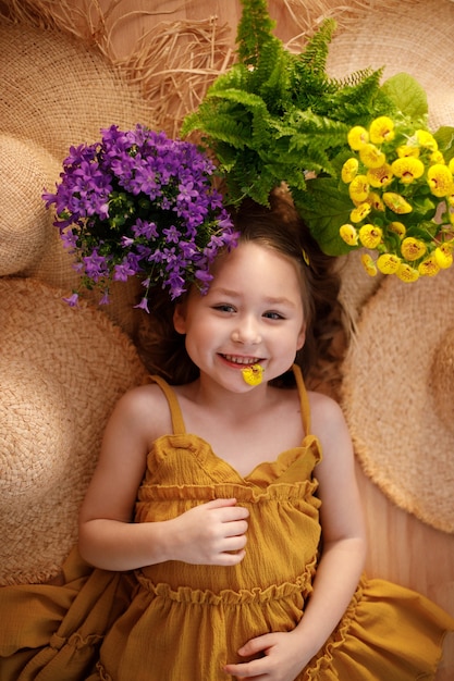 Portrait d'une petite fille allongée avec des fleurs et un chapeau de paille, concept de sentiment d'été et de voyage.