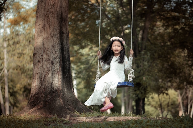 Portrait de petite fille asiatique jouant la balançoire sous le grand arbre dans la forêt naturelle avec ton vintage traité