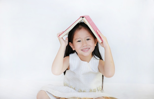 Portrait de petite fille asiatique place livre relié sur sa tête et regardant la caméra sur fond blanc.