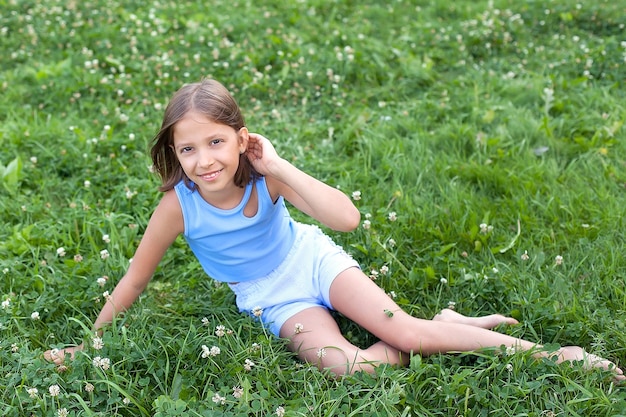 Portrait d'une petite fille assise sur l'herbe et redressant ses cheveux, il sourit et regarde la caméra