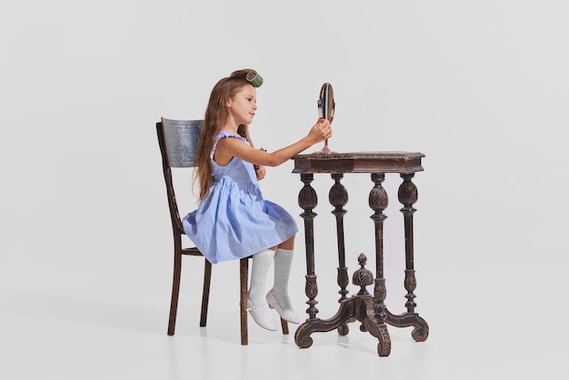 Portrait d'une petite fille assise à la table et se maquillant regardant sur un miroir isolé sur