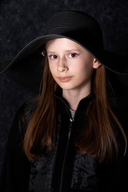 Portrait d'une petite fille au chapeau noir sur fond sombre.