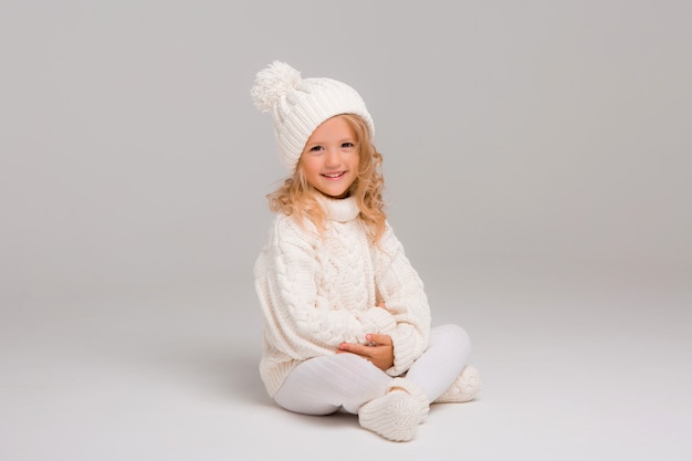 Portrait d'une petite fille aux cheveux bouclés dans un chapeau d'hiver blanc