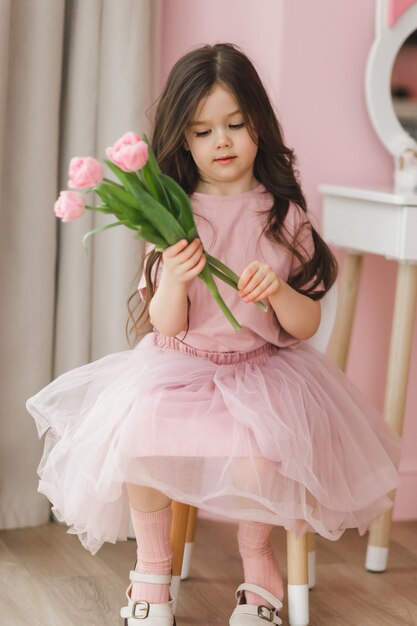 Portrait d'une petite fille aux longs cheveux noirs en gros plan Le bébé embrasse un bouquet de tulipes roses délicates fraîches Un cadeau pour les vacances de printemps