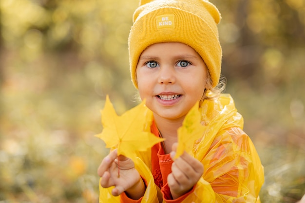 Portrait de petite fille aux yeux bleus au chapeau jaune avec des feuilles d'automne dans le parc