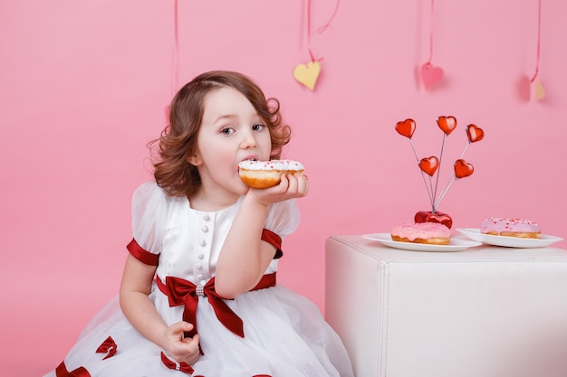 Portrait d'une petite fille avec un beignet dans ses mains sur rose