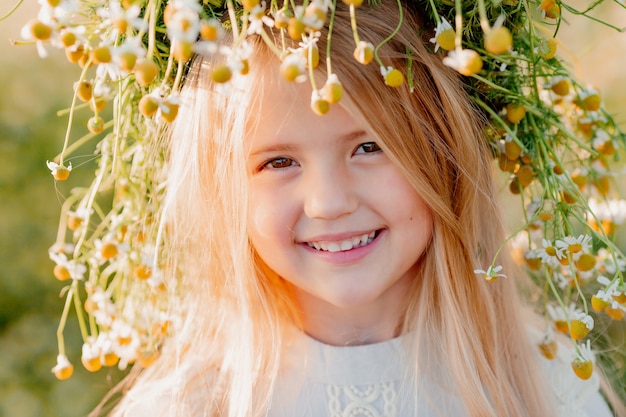 Portrait d'une petite fille blonde avec une couronne de marguerites sur la tête en été au coucher du soleil