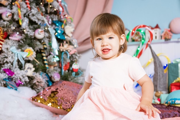 Portrait d'une petite fille blonde jouant près du sapin de Noël l'enfant porte un t-shirt blanc...