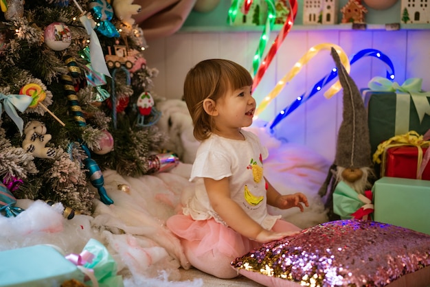 Portrait d'une petite fille blonde jouant près du sapin de Noël l'enfant porte un ts blanc...