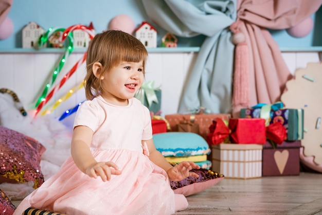 Portrait d'une petite fille blonde jouant près du sapin de Noël l'enfant porte un ts blanc...