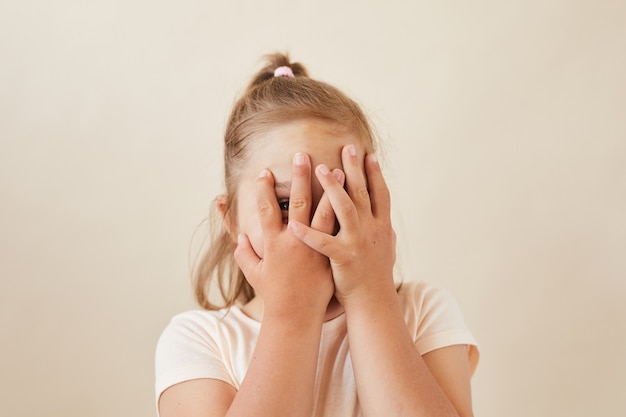 Portrait de petite fille cachant son visage avec les mains, elle joue à cache-cache isolé sur fond blanc