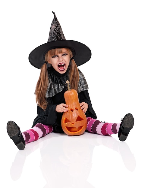 Portrait d'une petite fille avec un chapeau noir et une citrouille isolée sur un fond blanc