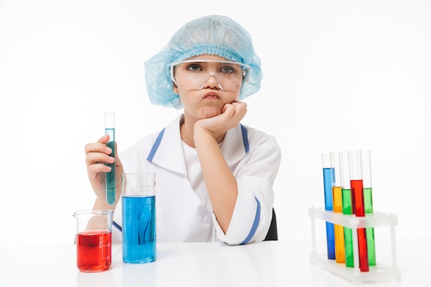 Portrait d'une petite fille ciblée en blouse blanche de laboratoire faisant des expériences chimiques avec un liquide multicolore dans des tubes à essai isolés sur un mur blanc