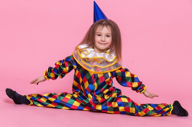 Portrait petite fille en costume de clown est assis sur une ficelle sur fond rose