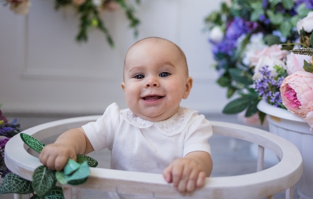 Portrait d'une petite fille dans un body blanc assis dans une arène sur fond de fleurs