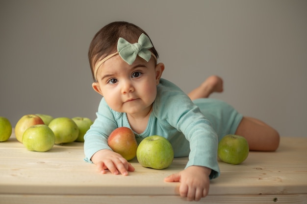 Portrait d'une petite fille dans un body vert sur une table en bois avec des pommes vertes fraîches. Produits naturels pour les enfants. photo de haute qualité