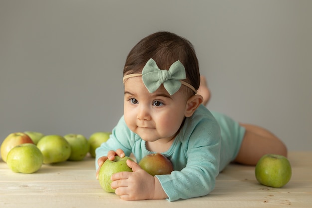 Portrait d'une petite fille dans un body vert sur une table en bois avec des pommes vertes fraîches. Produits naturels pour les enfants. photo de haute qualité