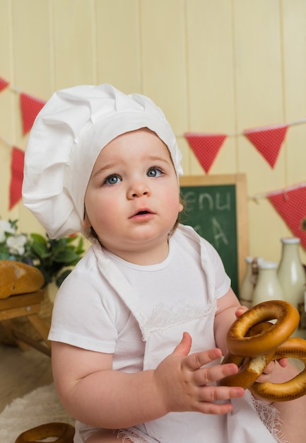 Portrait d'une petite fille dans un chapeau de chef tenant un bagel