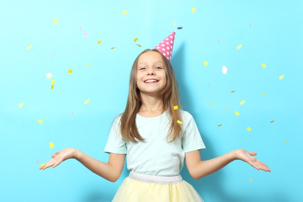 Portrait d'une petite fille dans un chapeau de fête sur un fond et des confettis colorés