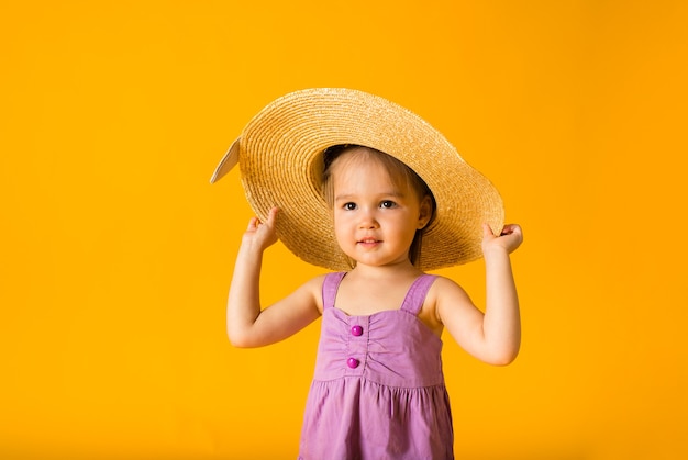 Portrait d'une petite fille dans une robe d'été et un chapeau de paille sur une surface jaune avec un espace pour le texte