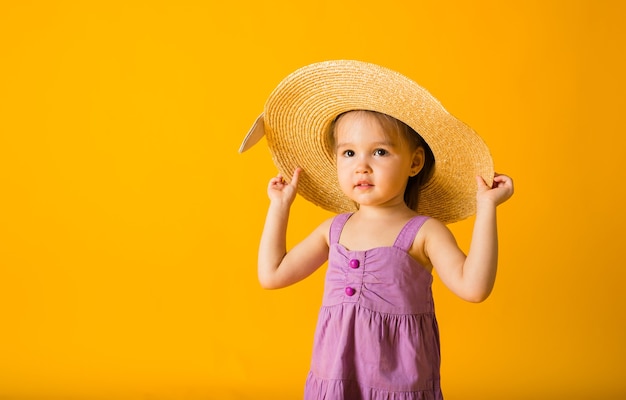 Portrait d'une petite fille dans une robe d'été violette et un chapeau de paille sur une surface jaune avec un espace pour le texte