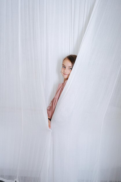 Photo portrait d'une petite fille debout derrière des rideaux blancs