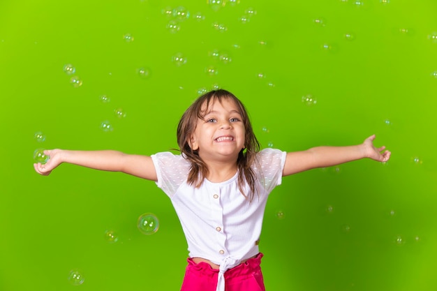 Portrait d'une petite fille gaie isolée sur fond vert soufflant des bulles de savon s'amusant